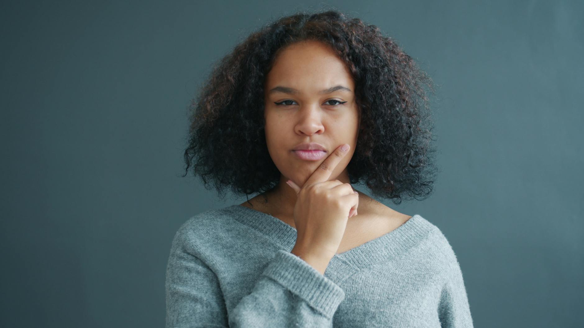 contemplative woman in gray sweater against gray background